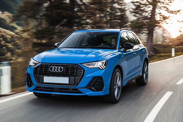 A blue Audi Q3 driving down a country road.